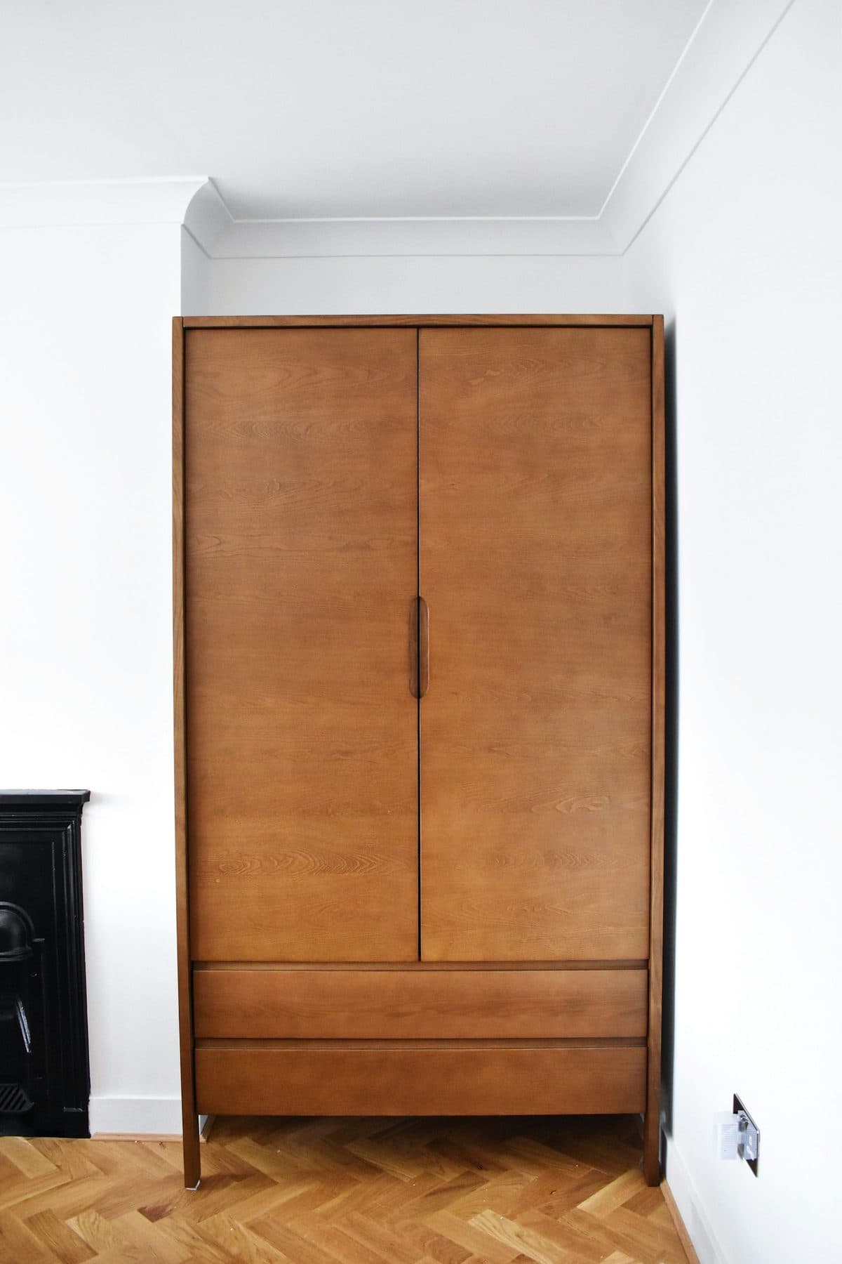 Tall wooden two-door wardrobe against a white bedroom wall