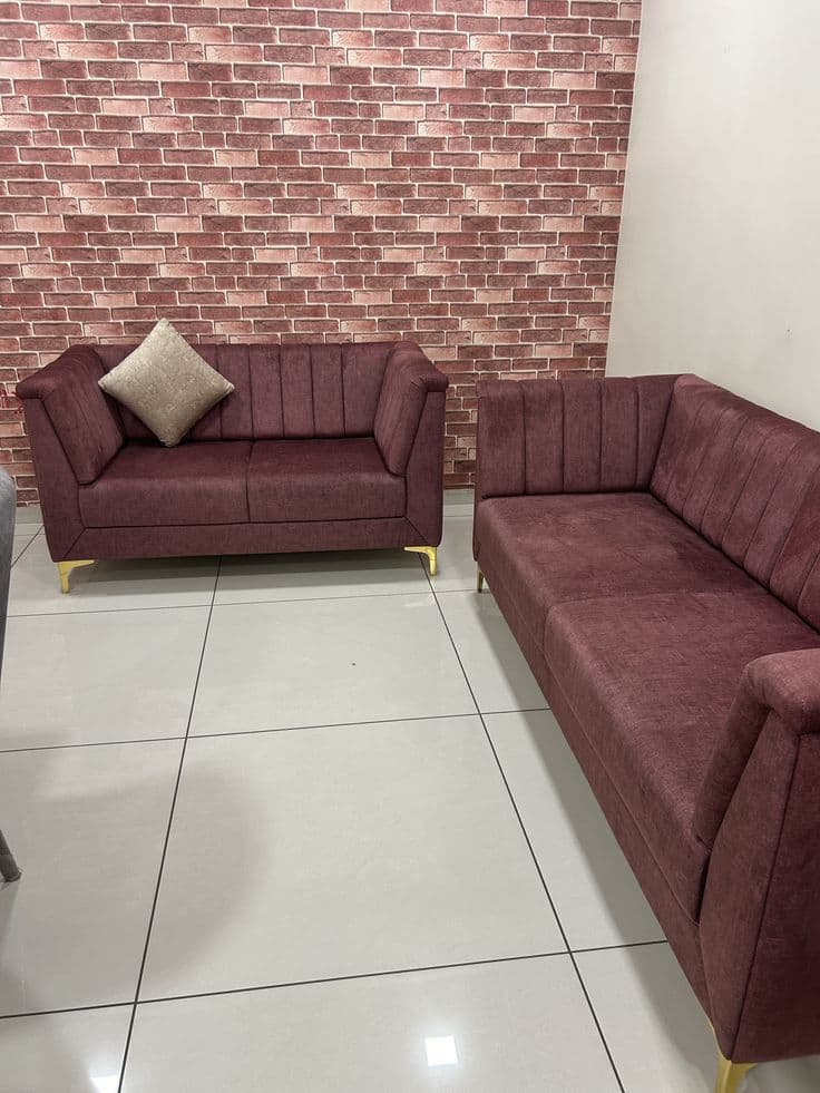Maroon channel-tufted sofa and loveseat against an exposed brick wall