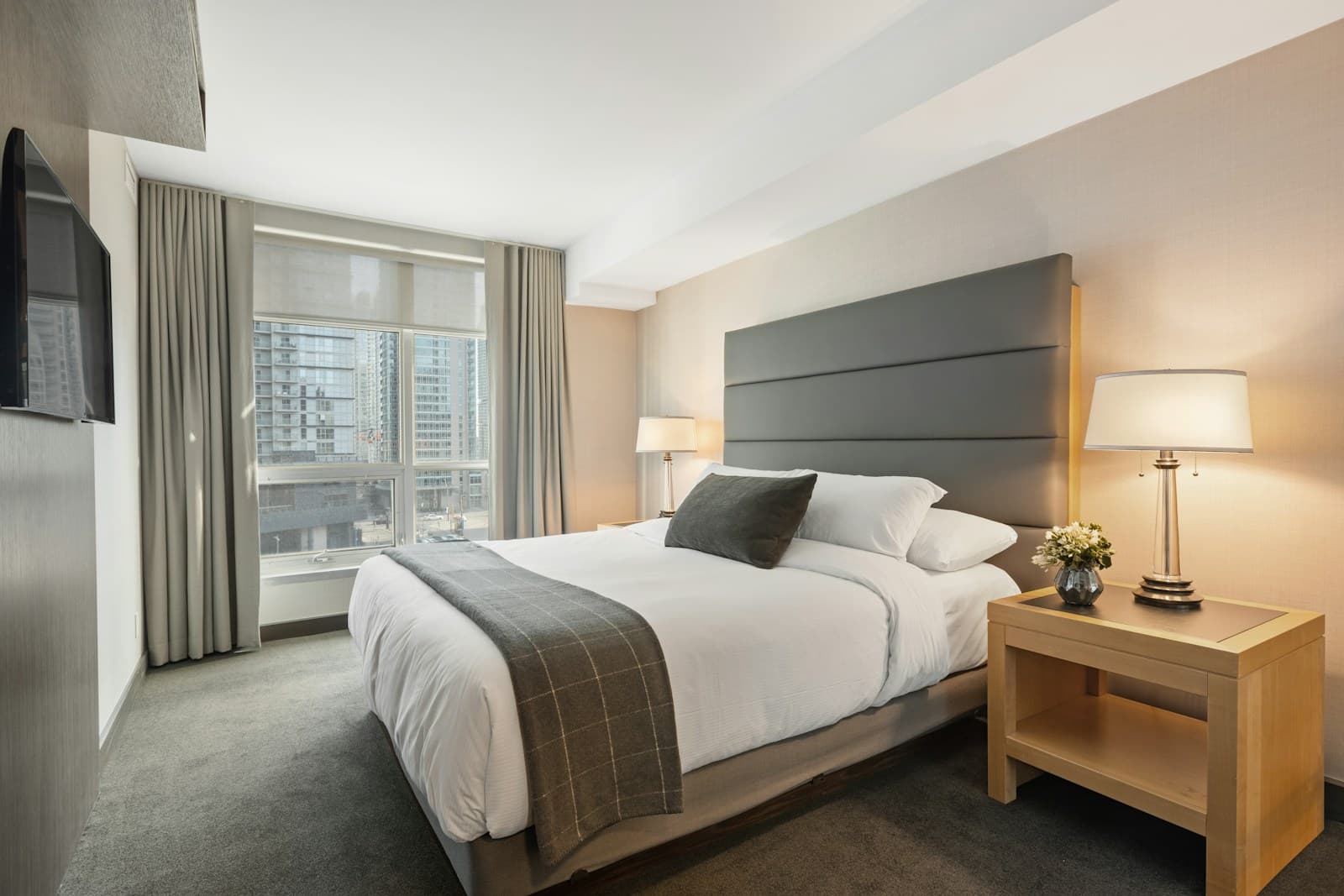 Hotel style bed with a wide panelled grey headboard and bedside table