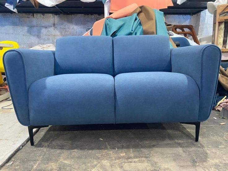 Slate blue two-seater sofa finished and staged in the workshop, upholstery rolls in the background