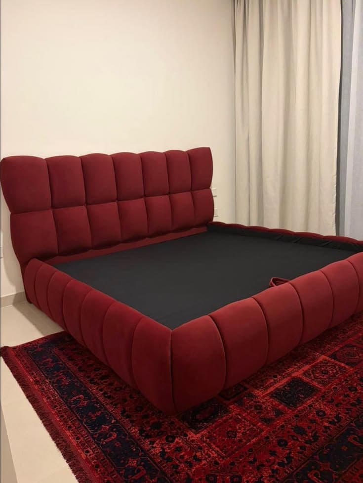 Deep red channel-tufted bed dressed on a patterned rug in a furnished bedroom