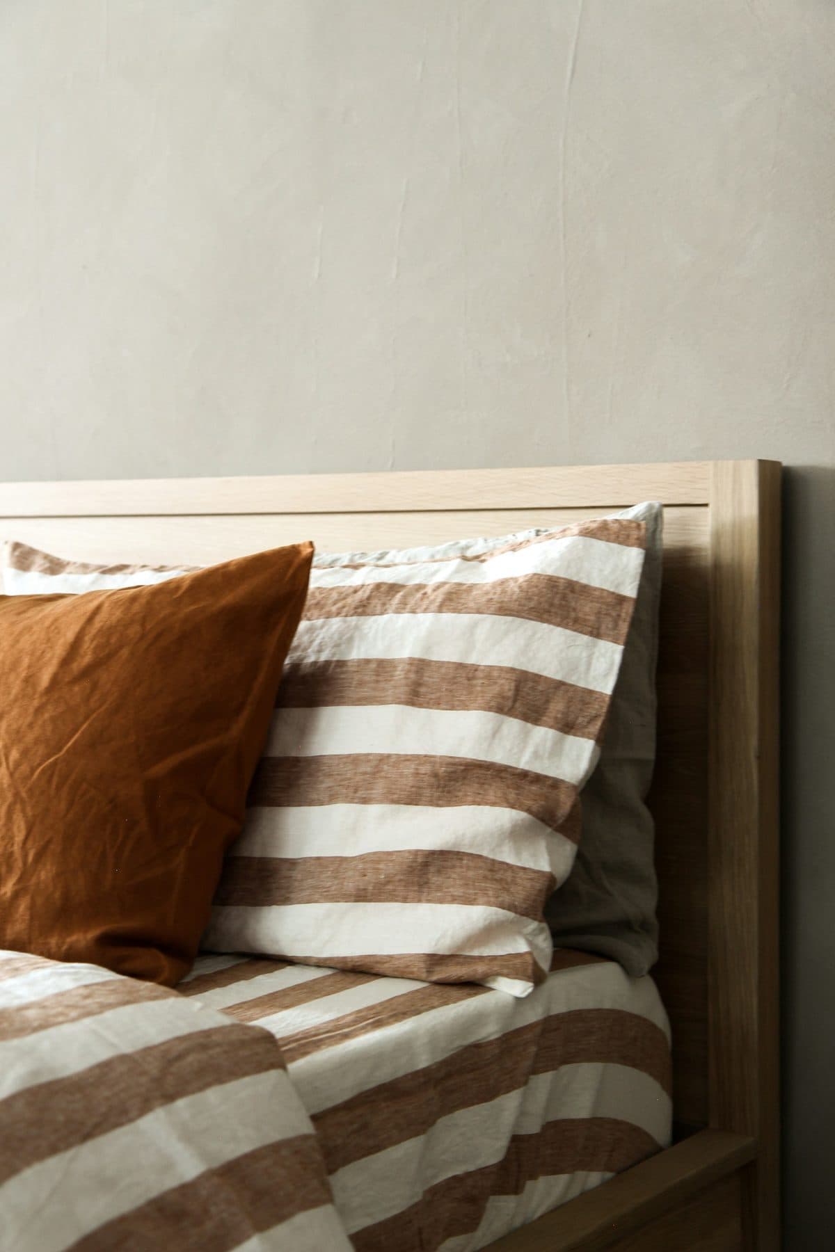 Close up of striped and plain linen bedding on an upholstered bed, showing the stitching